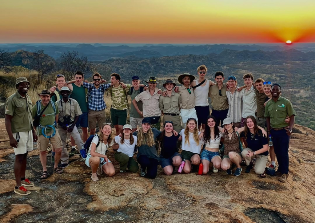 A safari group standing at the peak of a large kopje with the sunset behind them in Matobo National Parl